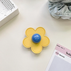 Macro shot of yellow leather flower phone grip with blue center on white marble table
