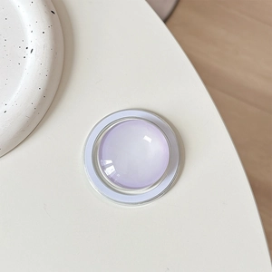 Close-up of a lilac crystal glass MagSafe phone grip on a minimalist desktop background