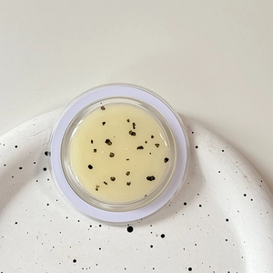 Detailed macro view of light yellow cream with dark particles in a round clear glass jar
