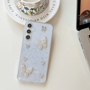 Detail of glittery blue phone case with pearl butterflies and metal rose on a ceramic plate