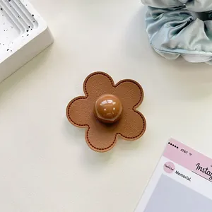 Macro detail of brown leather flower phone grip with stitching and center bead