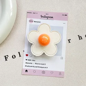 Detail of flower-shaped phone grip with cream petals and orange center on a card