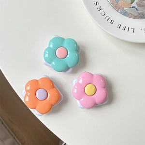 Close-up of three colorful flower-shaped phone mirror grips in mint, orange, and pink