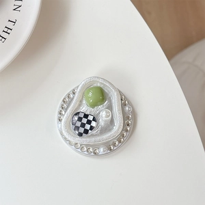 Close-up of heart phone grip with rhinestones, green gem, and pearls on a white surface