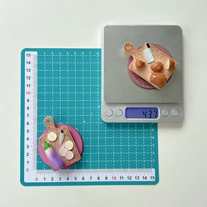 Miniature cutting board phone grip showing dimensions on a green mat and exact weight
