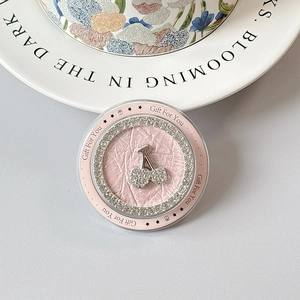 Close-up of pink leather phone grip with rhinestone cherry design in a floral ceramic dish