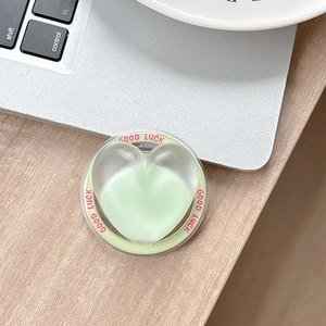 Detail of light green heart-shaped phone grip with Good Luck text on a wooden desk