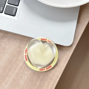 Detail of transparent heart phone grip with yellow 'GOOD LUCK' rim on a laptop