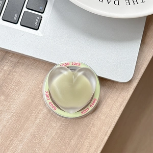Macro detail of a heart-shaped matte green phone grip with Good Luck pink text
