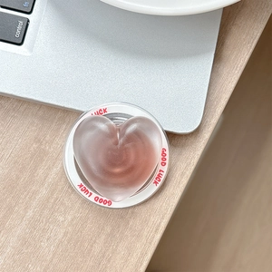 Close-up of a matte pink heart phone grip with Good Luck text on a wooden desk