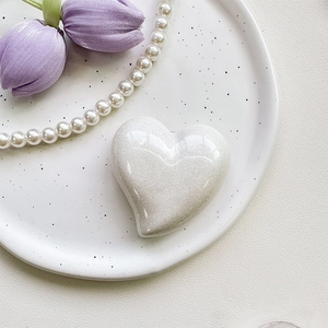 Detail of heart-shaped phone grip with white glitter finish and aesthetic pearly texture
