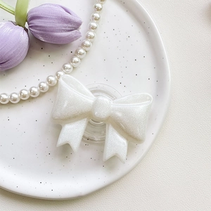 Detail of white glitter 3D bow phone socket stand on a ceramic plate with decor