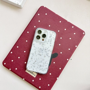 Dettaglio custodia iPhone trasparente con paillettes a stella su sfondo rosso a pois