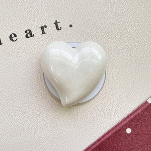 Close-up of white pearlescent heart phone grip with glitter finish on textured background