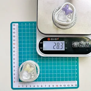 Detail view of heart-shaped phone grip with bow and pearls on a digital scale weighing 28.3g