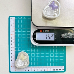 Close-up of butterfly resin phone stand showing dimensions and weight on a digital scale