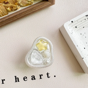 Dettaglio del supporto per telefono in resina con conchiglia e stella su pelle e terrazzo