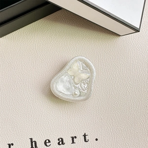 Close-up of heart-shaped pearls and butterfly inside a resin mobile phone grip stand