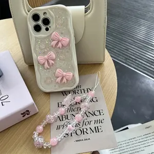 Detail of cream wavy iPhone case with pink bows, glitter, and a beaded phone charm strap