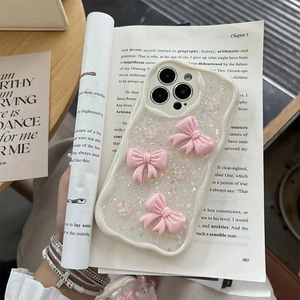 Glittery cream iPhone case with 3D pink bows and wavy edges on a book background