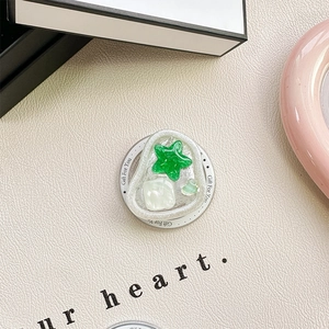 Detail of a transparent resin heart phone grip with green stars and pearl shell accents