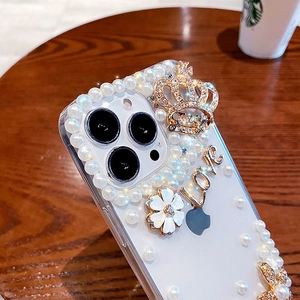 Macro detail of luxury phone case with pearls, gold crown, and LOVE charms on wood