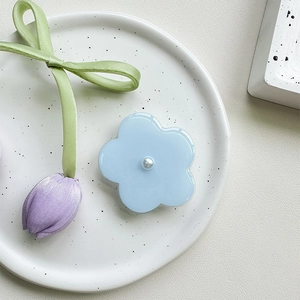 Macro shot of light blue floral phone grip with a white pearl center on a ceramic plate