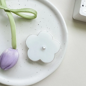 Detail of a white flower phone grip featuring a central pearl on a white ceramic plate