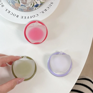 Tre contenitori per balsamo solido a forma di mela in rosa, verde e viola su tavolo