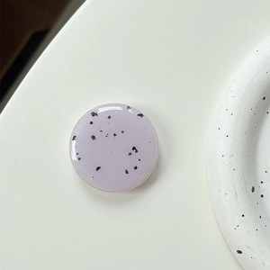 Close-up of a lavender phone grip with black ink spots on a minimalist background
