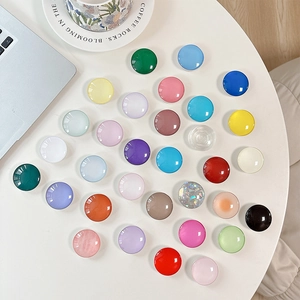 Variety of colorful round crystal glass pop socket phone grips on a white table