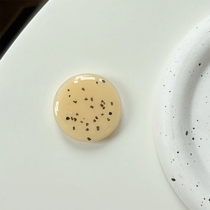 Close-up of minimalist beige resin phone grip with black flecks on a white ceramic plate