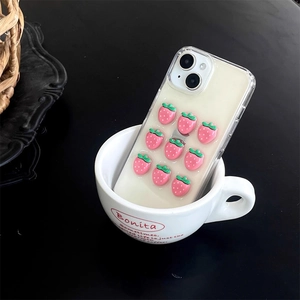Detail shot of 3D pink strawberry charms on clear iPhone case inside a white mug