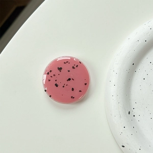 Close-up of a round pink popsocket with black speckles on a minimalist display tray
