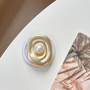 Detail of matte gold oval phone socket with a large pearl center on a white surface