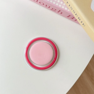Close-up of soft pink cream blush in a round vibrant pink case on a clean white desk