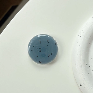 Detail view of round blue-gray phone grip with black speckled texture on white background