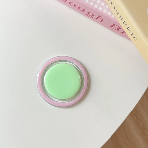 Detail shot of a pastel green and pink collapsible phone grip on a white minimalist desk