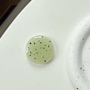 Macro detail of round light green resin phone grip with minimalist black speckle pattern