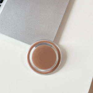 Top view of a round magnetic phone stand in brown cream finish on a laptop desk surface