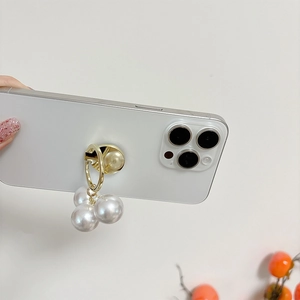 Detail of a gold metal phone ring holder with three hanging white pearls on a white phone