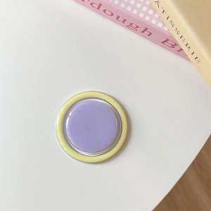 Flat lay of a pastel lavender and yellow round phone socket grip on a white desk