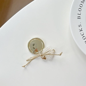 Detailed view of gold mirror phone grip with pearls, bow, and heart pendant decoration