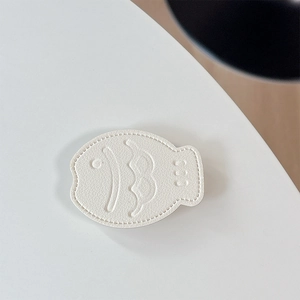 Detailed view of white fish-shaped leather phone stand with lychee grain and stitching
