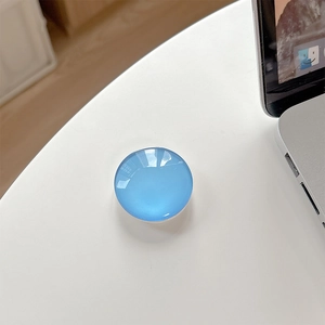 Detail of a round sky blue crystal glass phone grip with glossy finish on a desk