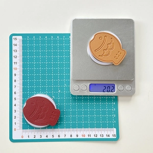 Close-up of fish-shaped leather phone grips on a scale showing 20.2g weight and size