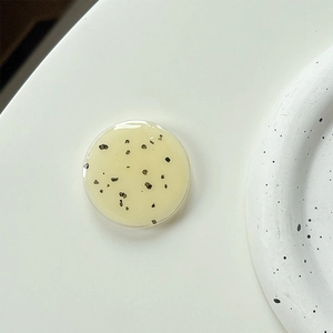 Close-up of minimalist beige resin phone grip with black flecks on a white surface