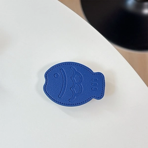 Macro view of dark blue leather fish-shaped phone grip with fine lychee texture and stitching