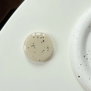 Macro detail of glossy cream-colored round phone grip with minimalist black speckles
