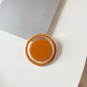 Detail of a round orange magnetic phone grip with acrylic edges on an office desk